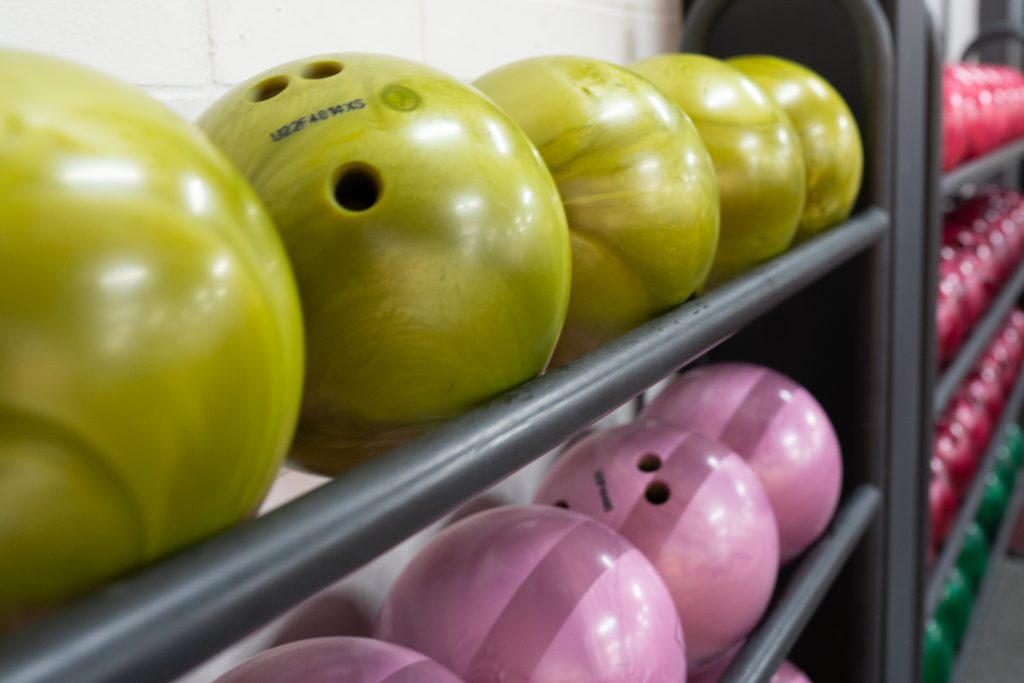 Green and purple bowling balls on a rack at a bowling alley.